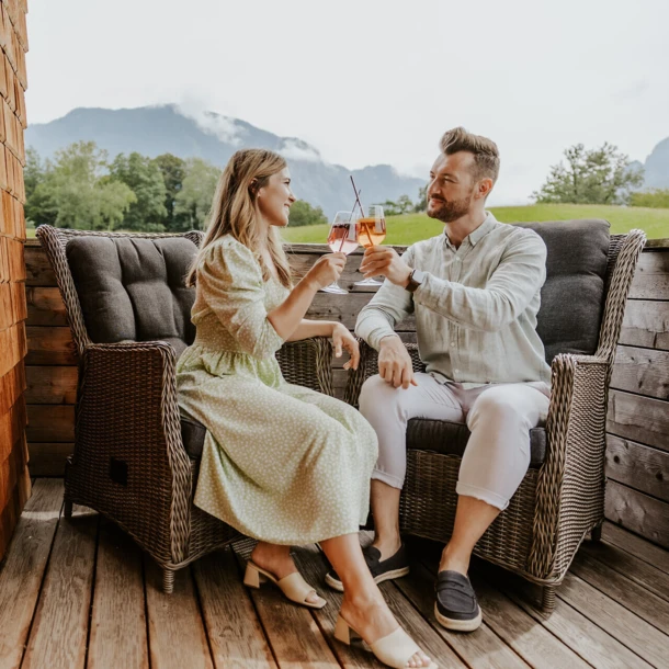 Ein Paar stößt mit Drinks in einem gemütlichen Außenbereich des Hotel Klosterhof an, umgeben von Alpenlandschaft in Bayern.