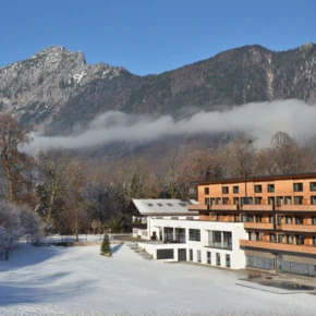 Hotel Klosterhof surrounded by snow-covered trees and mountains under a clear blue sky.