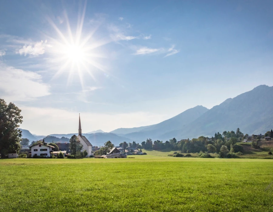 Sonnenstrahlen über dem Hotel Klosterhof in Bayerisch Gmain, umgeben von grünen Wiesen und Bergen im Hintergrund.