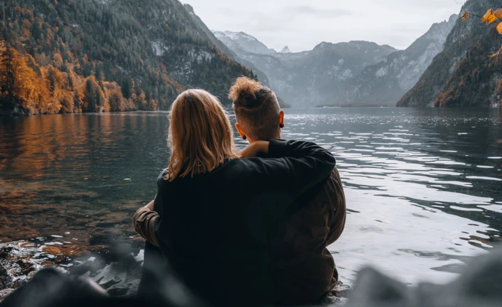 Ein Paar sitzt umarmt am See mit Blick auf die Herbstlandschaft und Berge.