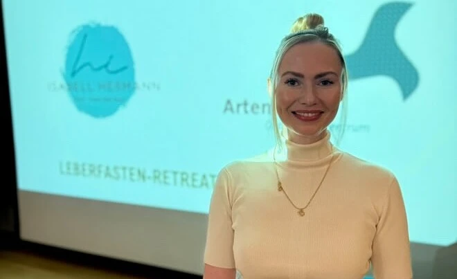 Eine Frau steht lächelnd vor einer Präsentation mit "Leberfasten-Retreat" im Hotel Klosterhof.