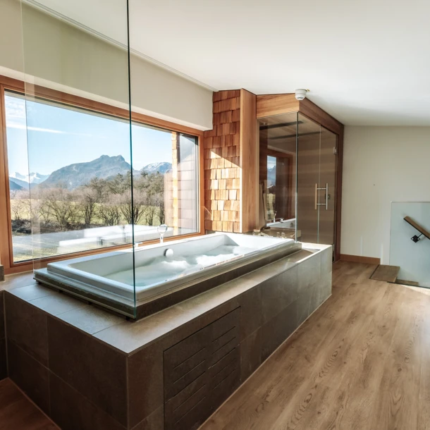 Junge Dame im Whirlpool mit Rosenblättern und Blick aus dem Panoramafenster im Hotel Klosterhof, Bayern.