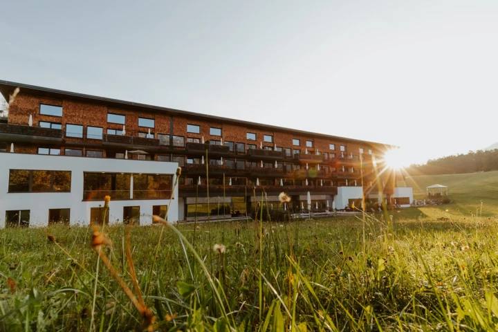 Moderne Fassade des Hotel Klosterhof in Bayerisch Gmain, umgeben von Wiese und Alpen bei Sonnenuntergang. Wellnesshotel mit alpinem Charme.