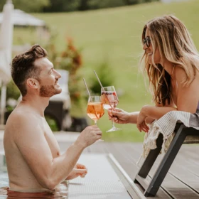 Ein Paar prostet sich mit Cocktails am Pool zu, umgeben von einer malerischen Landschaft. Entspannte Atmosphäre und Sommerfreude.