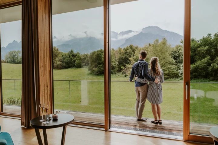 Ein Paar genießt die Aussicht auf die Alpen von ihrem Zimmer im Hotel Klosterhof, umgeben von Natur und Ruhe.