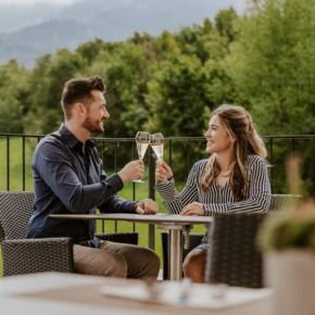 Ein Paar steht auf dem Balkon ihres Hotelzimmers und genießt den Ausblick auf die Bergwelt im Berchtesgadener Land.