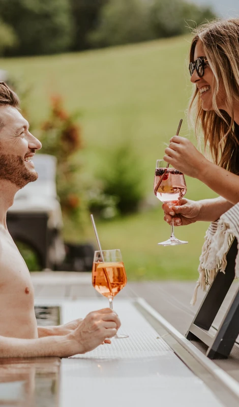 Ein Mann und eine Frau genießen Cocktails am Pool im Hotel Klosterhof, umgeben von einer grünen Landschaft in Bayern.